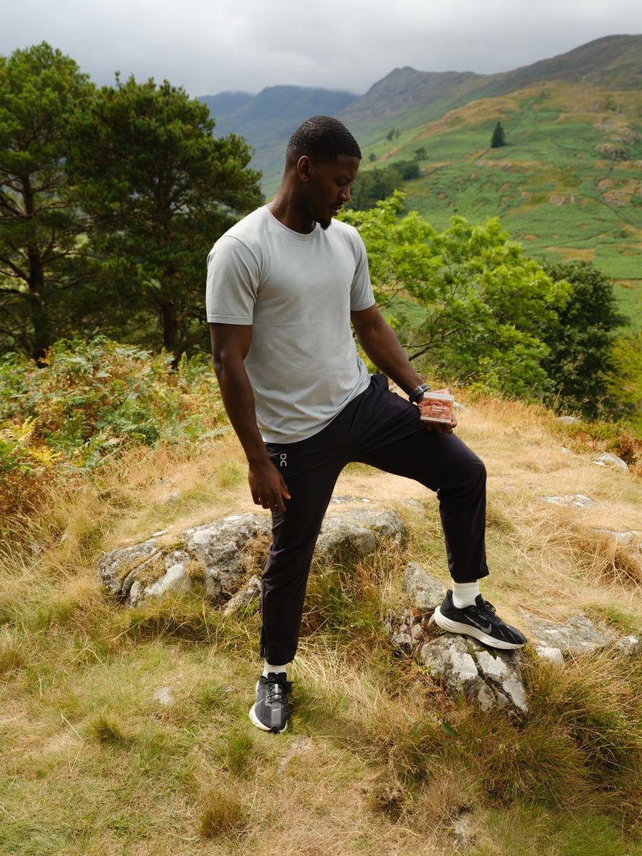 A man standing on a hillside with a tub of Creatine Chews in his hand