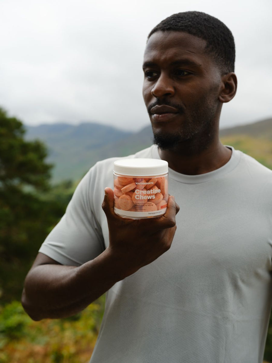 A man holding up a tub of Creatine Chews, looking out over the hills