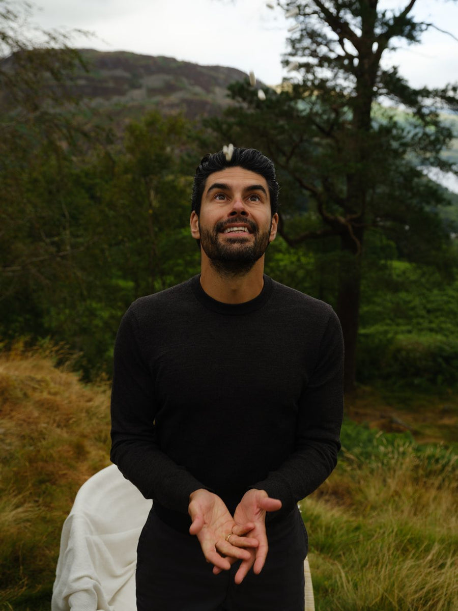 A man looking up and smiling as he tosses a chew into his mouth on a wooded hillside
