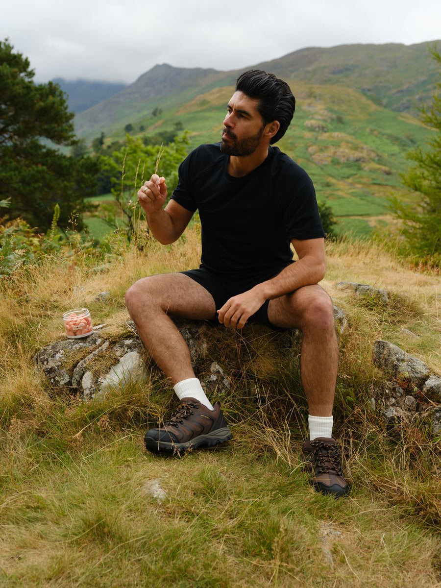 A man sitting on a rock with a chew in his hand and a tub beside him