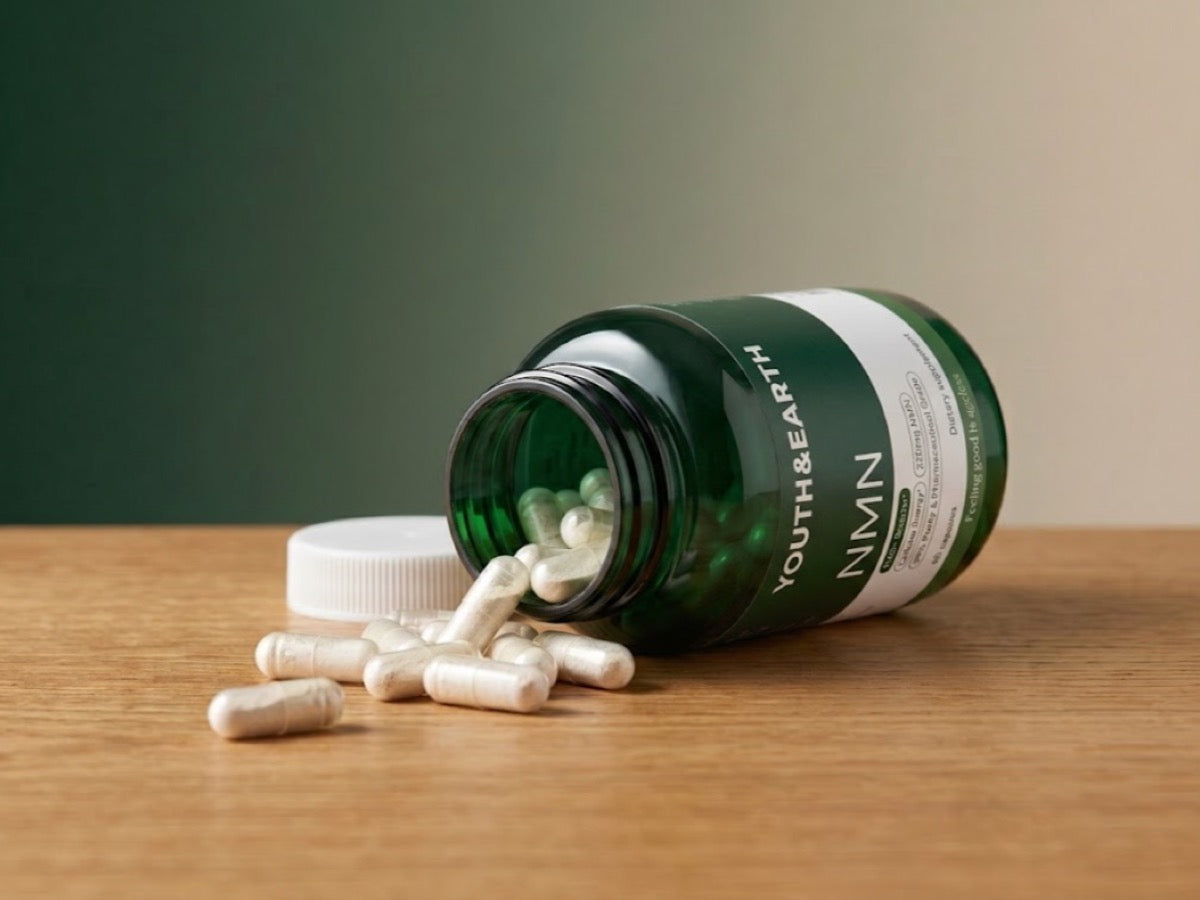 Youth & Earth NMN bottle tipped over with capsules spilling onto a wooden table