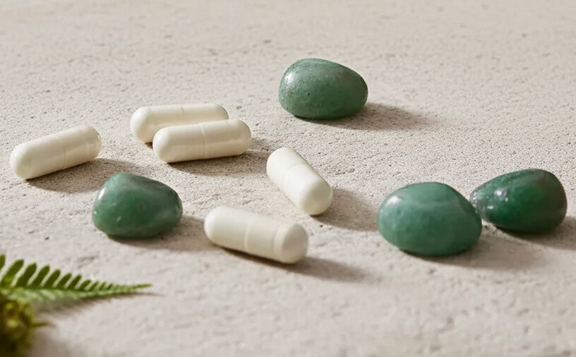 White capsules and green stones on a textured surface with a leaf.